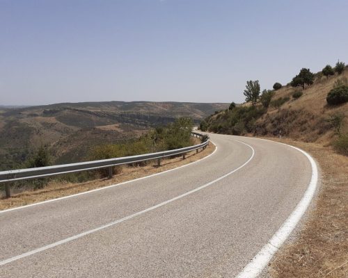 Carretera serpenteante en la montaña con vistas panorámicas de colinas y valles bajo un cielo despejado.