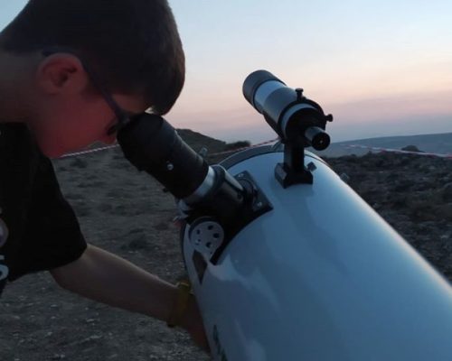 Niño observando a través de un telescopio durante el atardecer en una sesión de astronomía.