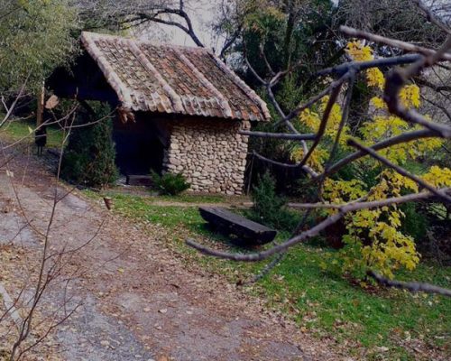 Vista de un camino de tierra con una pequeña caseta de roca y un banco para sentarse al lado.