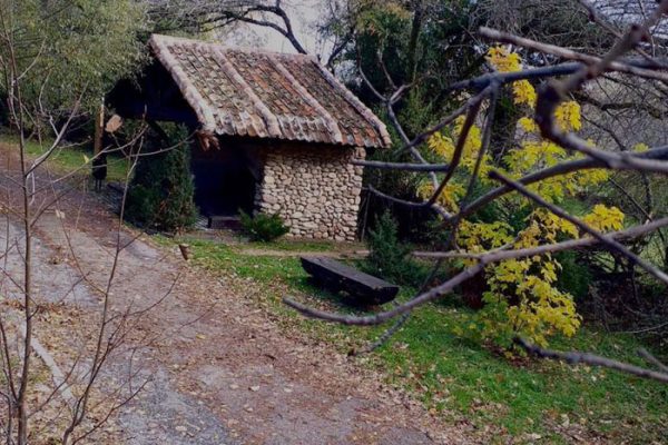 Vista de un camino de tierra con una pequeña caseta de roca y un banco para sentarse al lado.