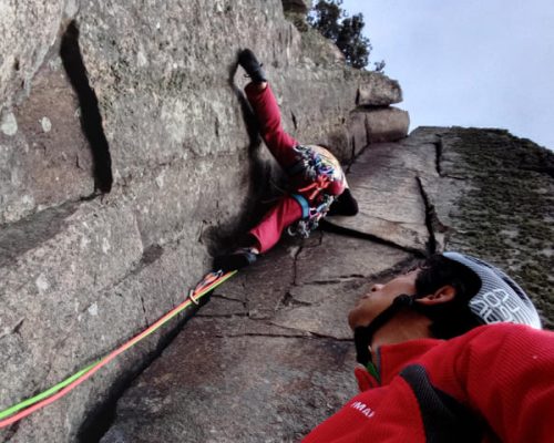 Guía de escalada asistiendo a un escalador en una pared rocosa.