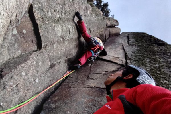 Guía de escalada asistiendo a un escalador en una pared rocosa.